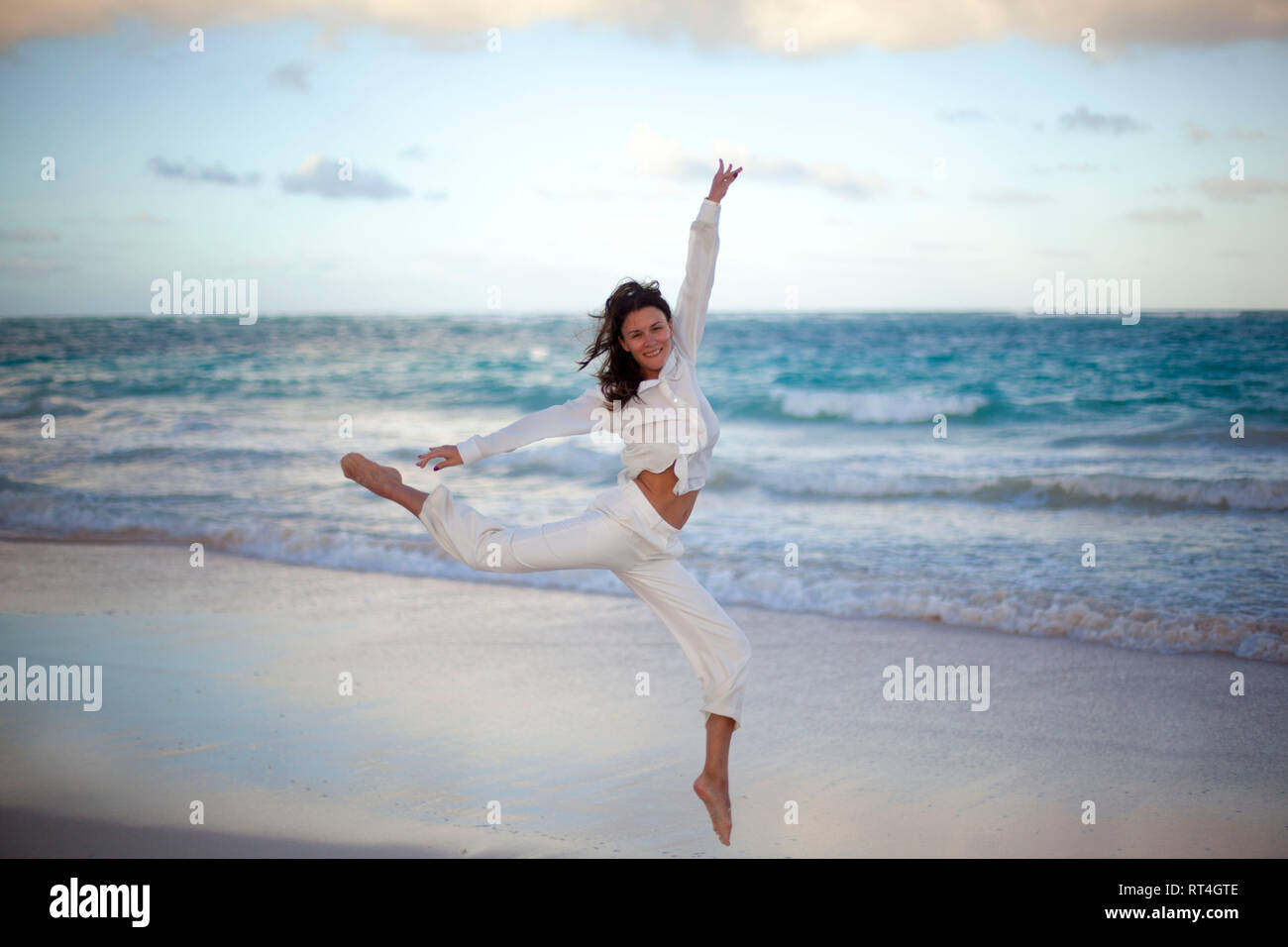 Jeune femme belle danse portant des vêtements blancs de même le coucher du soleil à tropical beach Banque D'Images