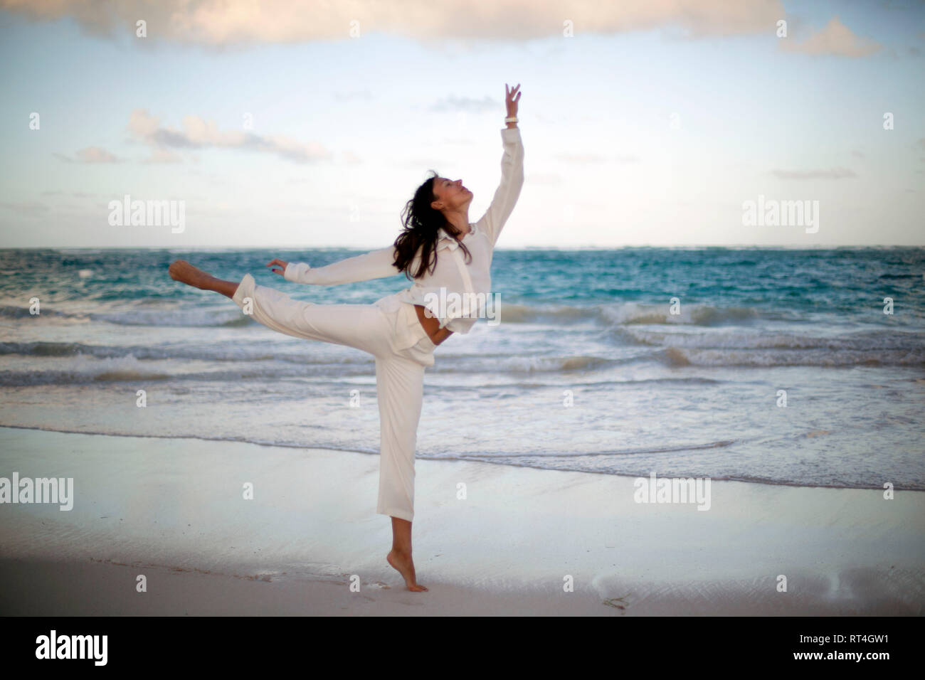 Jeune femme belle danse portant des vêtements blancs de même le coucher du soleil à tropical beach Banque D'Images