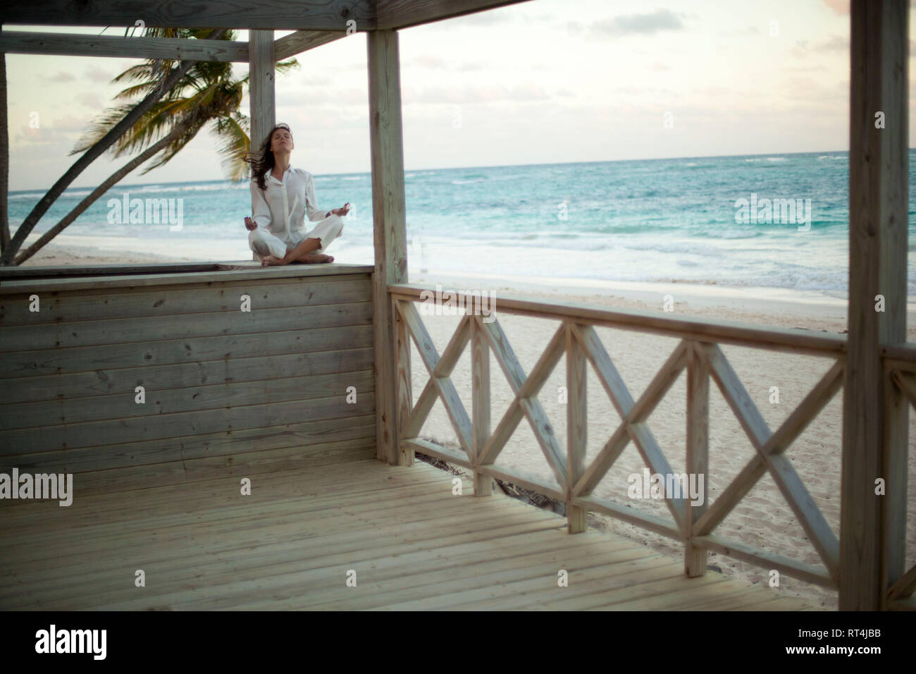 Une belle jeune femme en blanc cherche sa paix au coucher du soleil dans une plage tropicale Banque D'Images