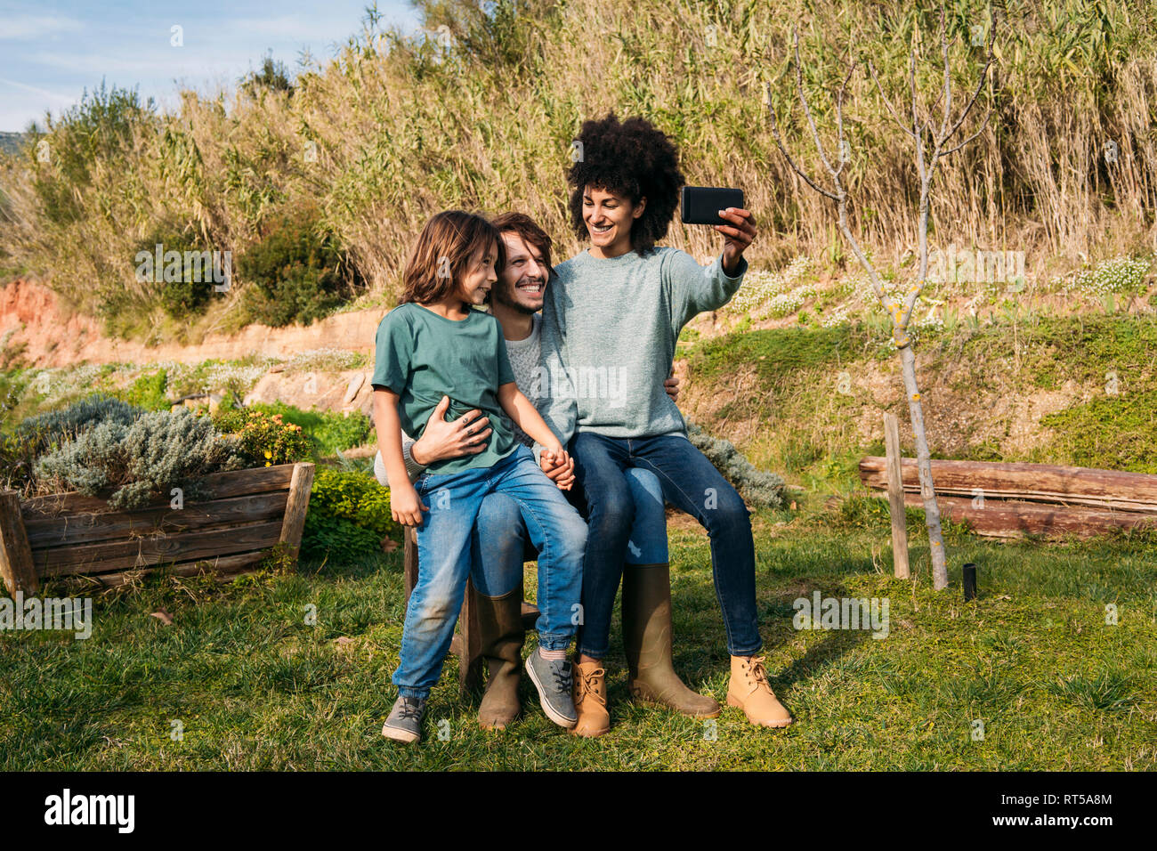 Famille heureuse assis sur un banc dans un jardin, la mère en tenant vos autoportraits Banque D'Images