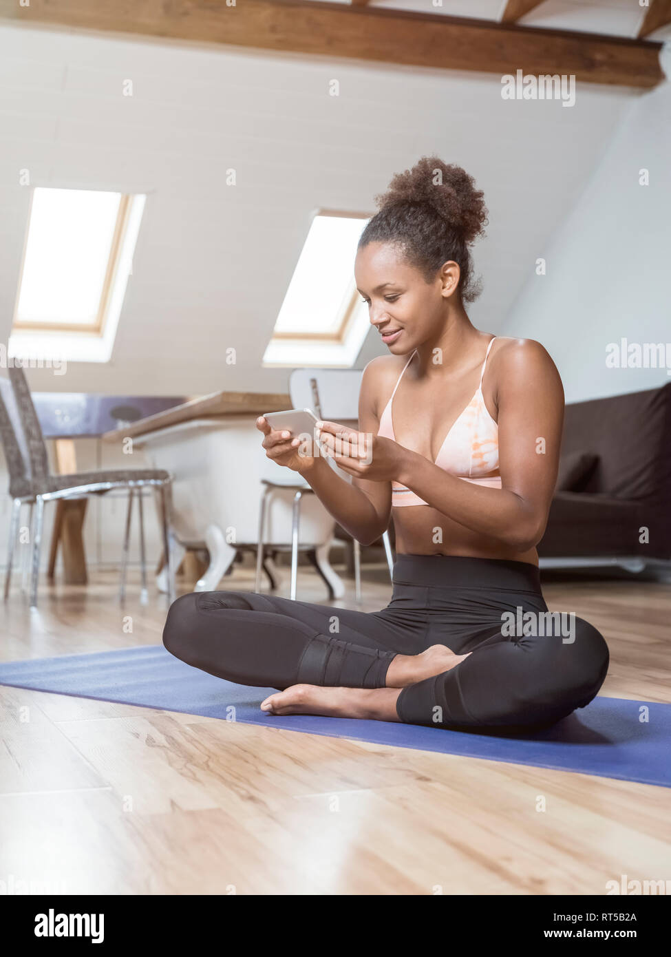 Jeune femme assise sur un tapis de yoga using cell phone Banque D'Images