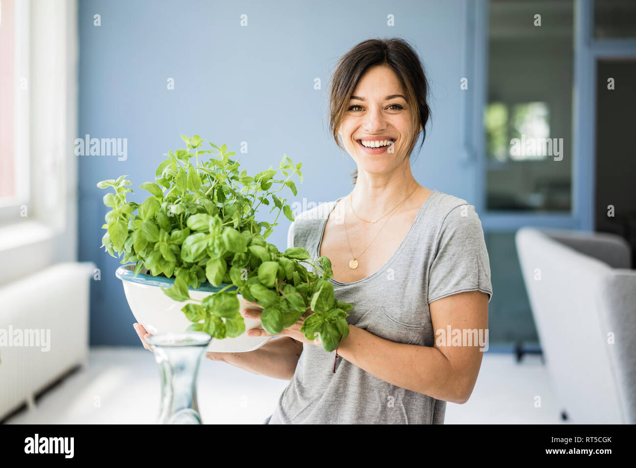 Femme debout dans la cuisine, holding pot de basilic Banque D'Images Femme debout dans la cuisine, holding pot de basilic Banque D'Images