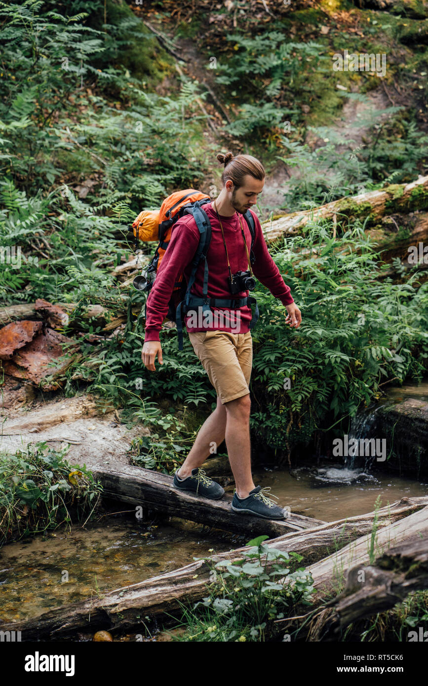 Young hiker with backpack traversant l'eau dans la forêt Banque D'Images