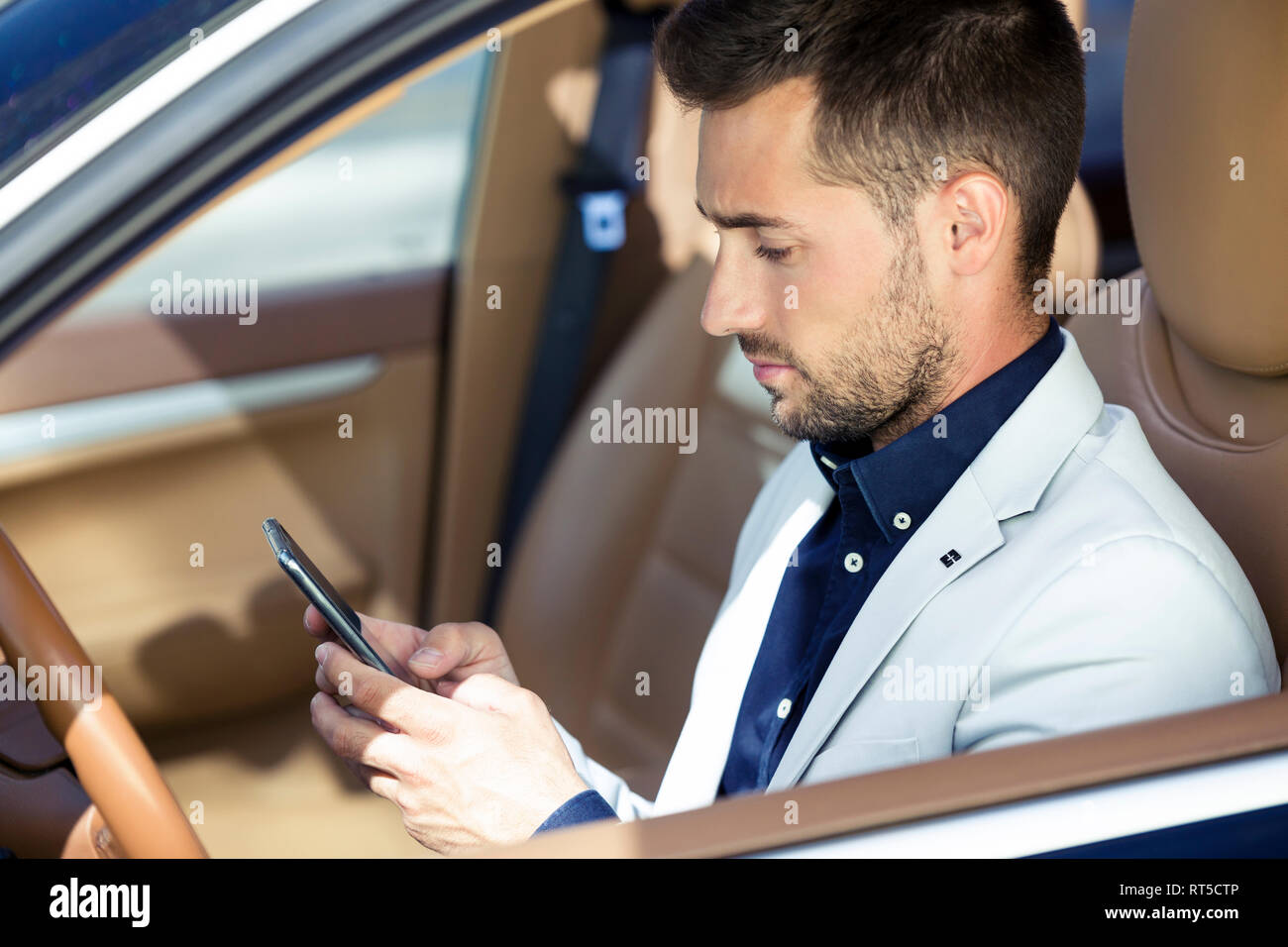 Young businessman sitting in car, using smartphone Banque D'Images