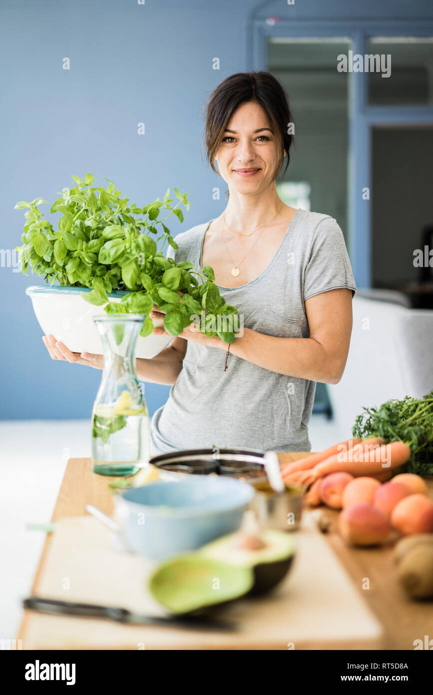 Femme debout dans la cuisine, holding pot de basilic Banque D'Images Femme debout dans la cuisine, holding pot de basilic Banque D'Images