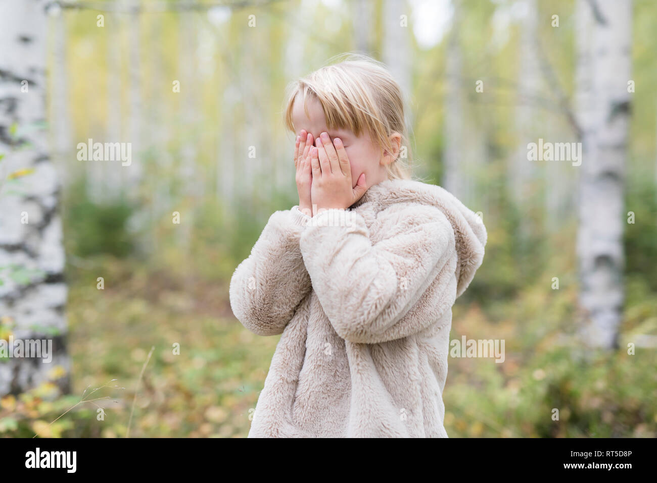 Fille blonde joue à cache-cache dans une forêt Banque D'Images