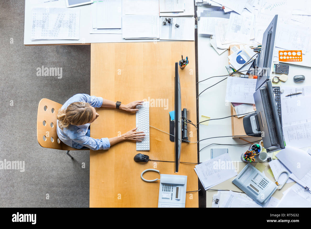 Vue de dessus de woman using computer at desk in office entouré par des documents Banque D'Images