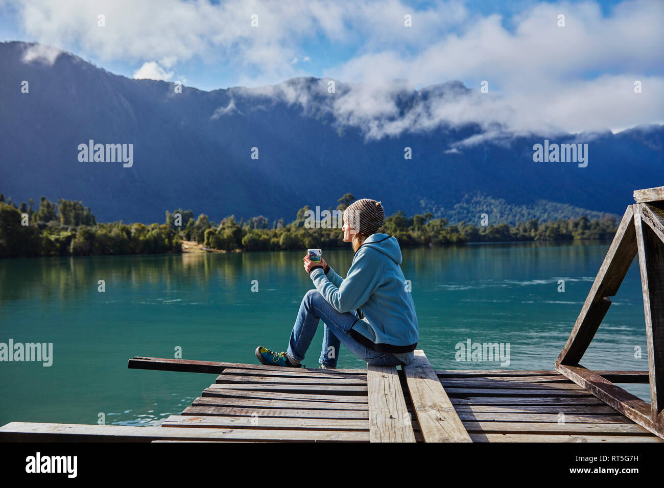 Chili, Lago Rosselot, Chaiten, woman sitting on jetty holding mug Banque D'Images