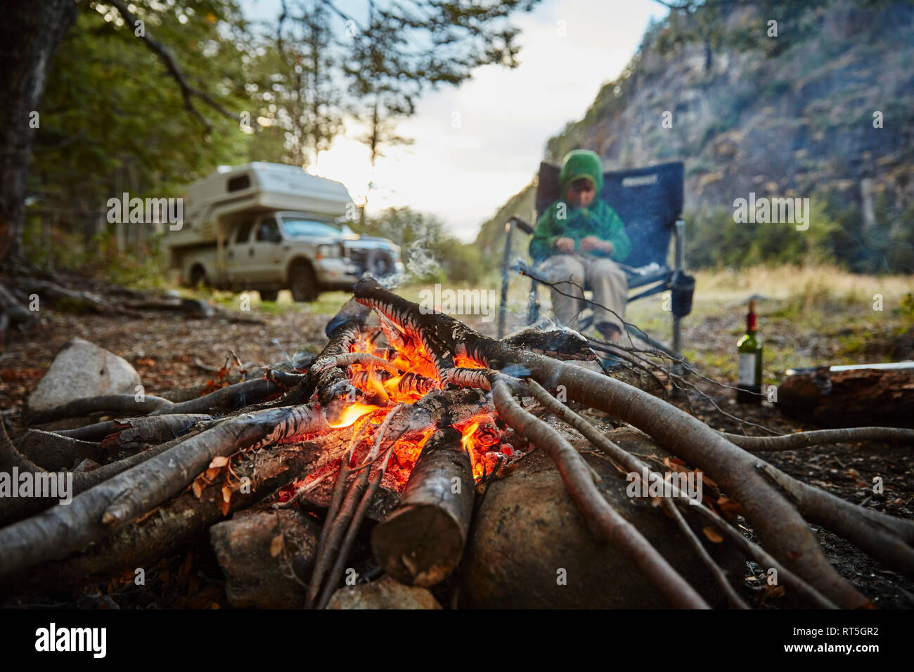Le Chili, Santa Magda, Rio, Maniguales garçon assis au feu de forêt avec le camping-car en arrière-plan Banque D'Images