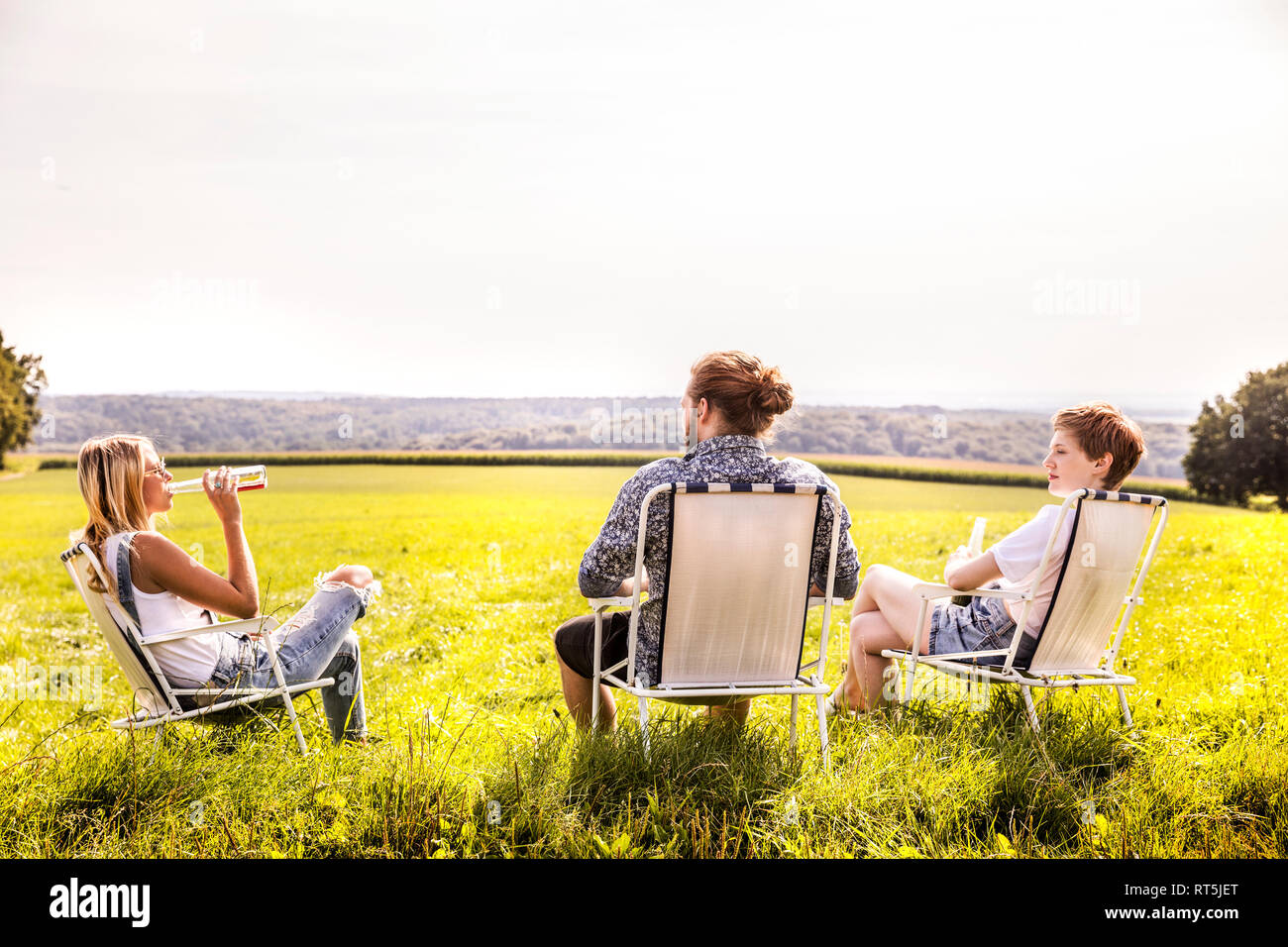 Amis assis sur les chaises de camping in rural landscape Banque D'Images