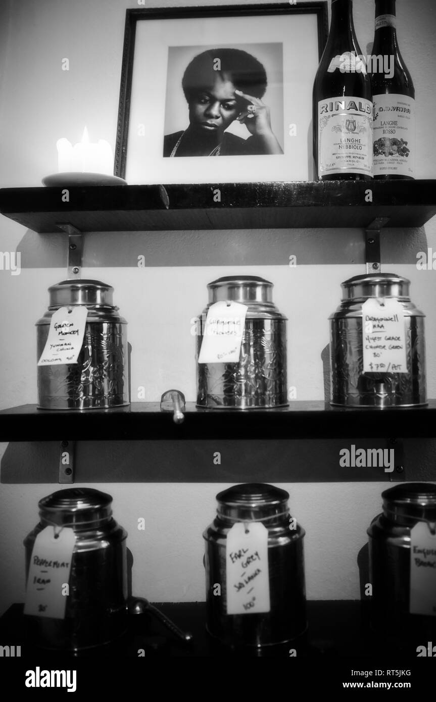 Un groupe de récipients contenant du thé en feuilles. Au-dessus se trouve une étagère avec une bougie, un portrait de Nina Simone et quelques bouteilles de vin. Banque D'Images