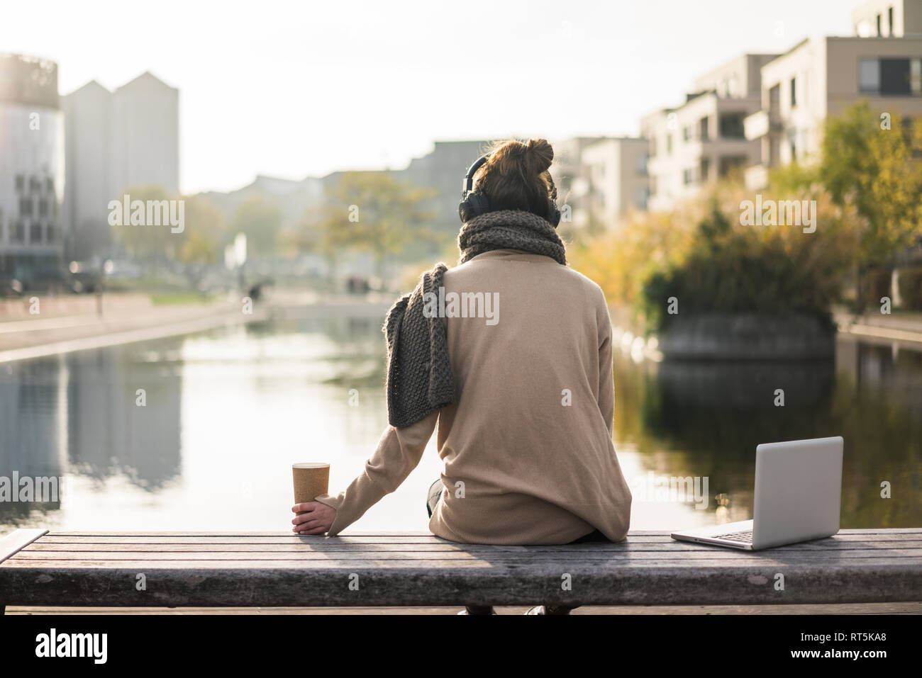 Vue arrière de femme assis sur un banc avec coffre et du café d'aller à l'écoute de la musique avec des écouteurs Banque D'Images