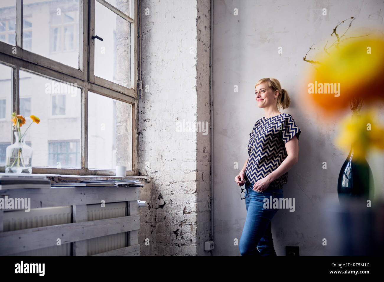 Smiling woman leaning against wall in loft à la recherche d'une fenêtre Banque D'Images