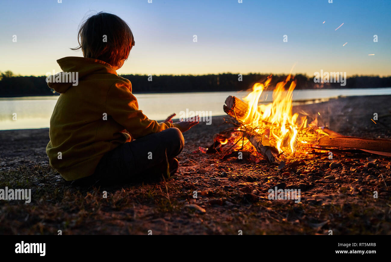 L'Argentine, Patagonie, Concordia, garçon assis au feu de camp au bord d'un lac Banque D'Images