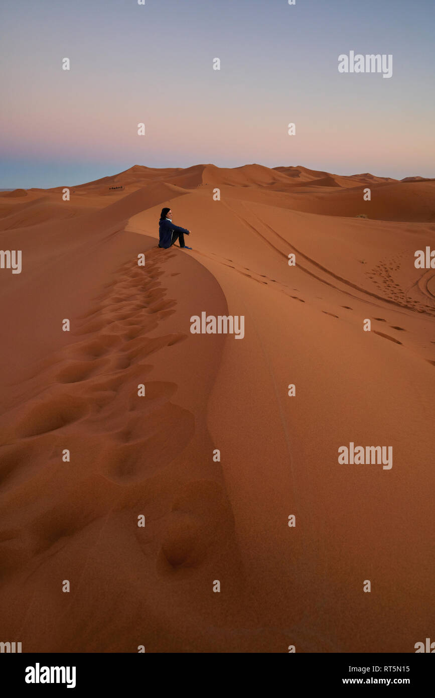 Maroc, femme assise sur des dunes du désert au crépuscule Banque D'Images