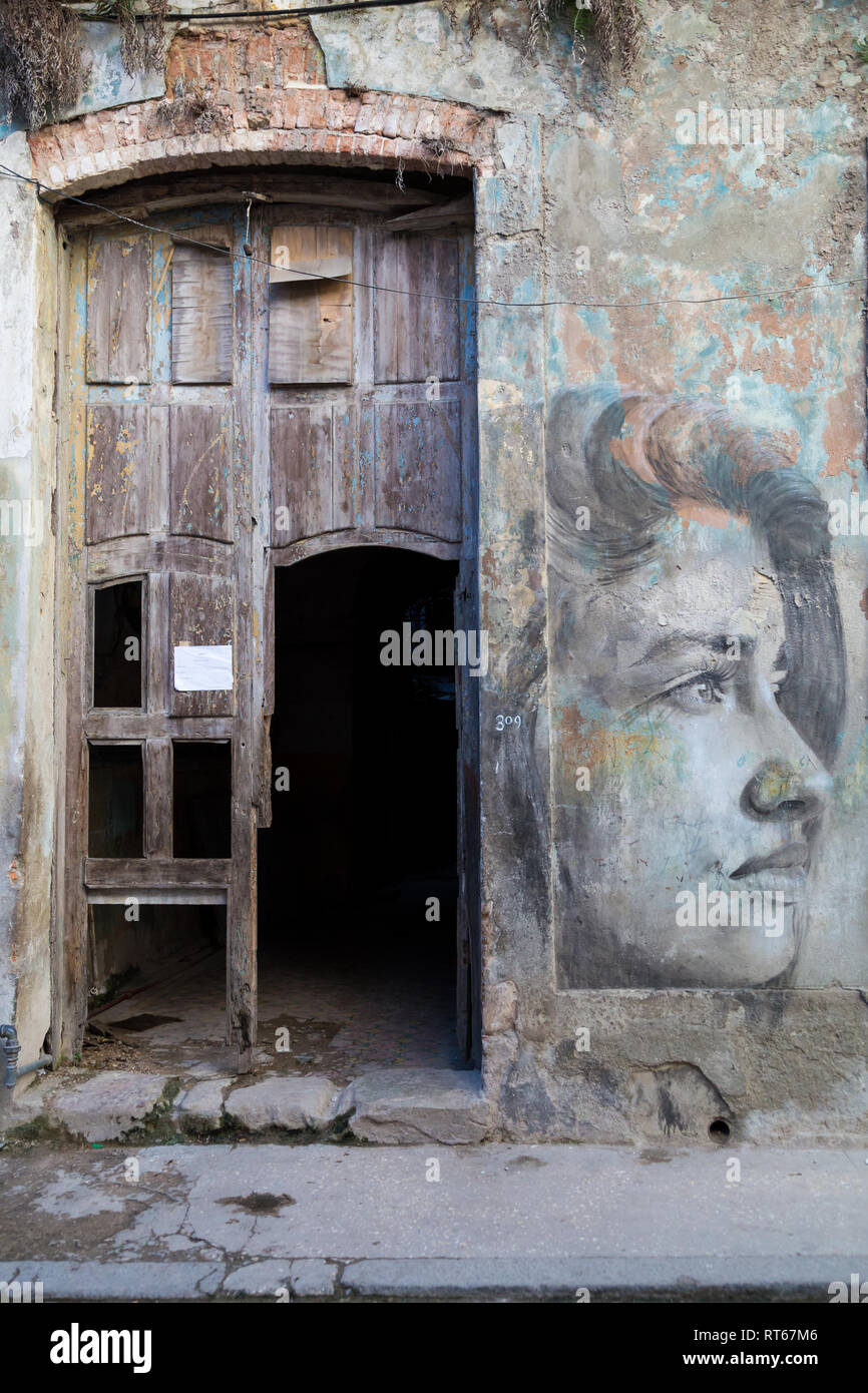 Entrée d'une chambre avec une porte cassée et les murs d'un mauvais état avec une peinture murale d'un visage de femme sur le côté droit. La Havane, Cuba Banque D'Images