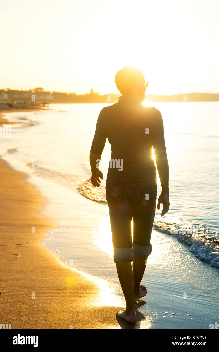 Silhouette d'homme qui marche sur la plage au coucher du soleil Banque D'Images