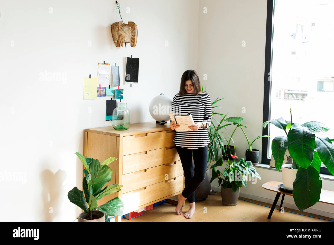 Jeune femme debout à une commode à la maison Lire un livret Banque D'Images Jeune femme debout à une commode à la maison Lire un livret Banque D'Images