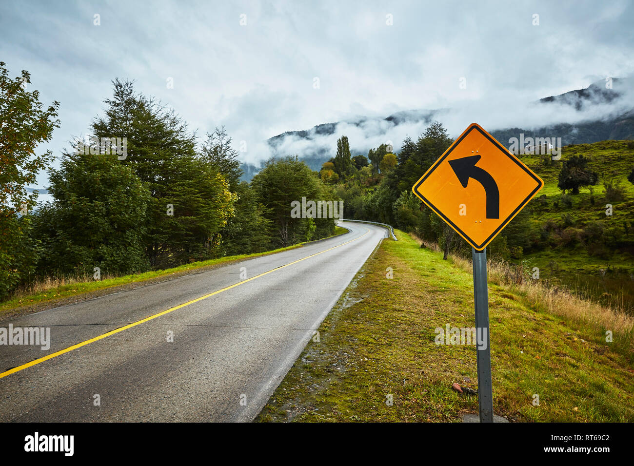 Le Chili, Puerto Aysen, route de campagne en automne avec curve road sign Banque D'Images