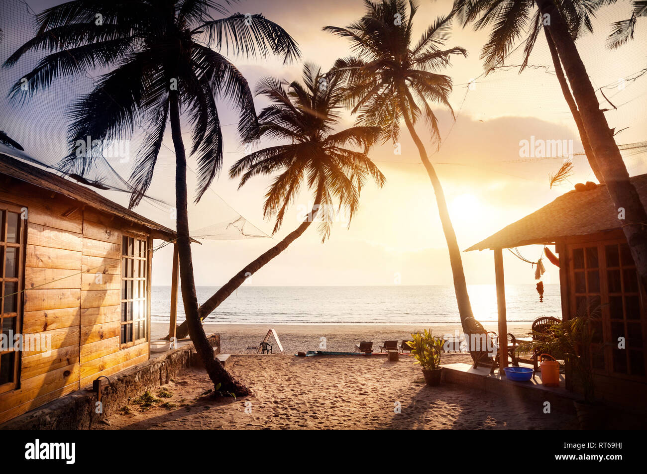 Chalet en bois avec vue sur la mer en complexe hôtelier tropical avec des cocotiers et des transats sur la plage au coucher du soleil Banque D'Images