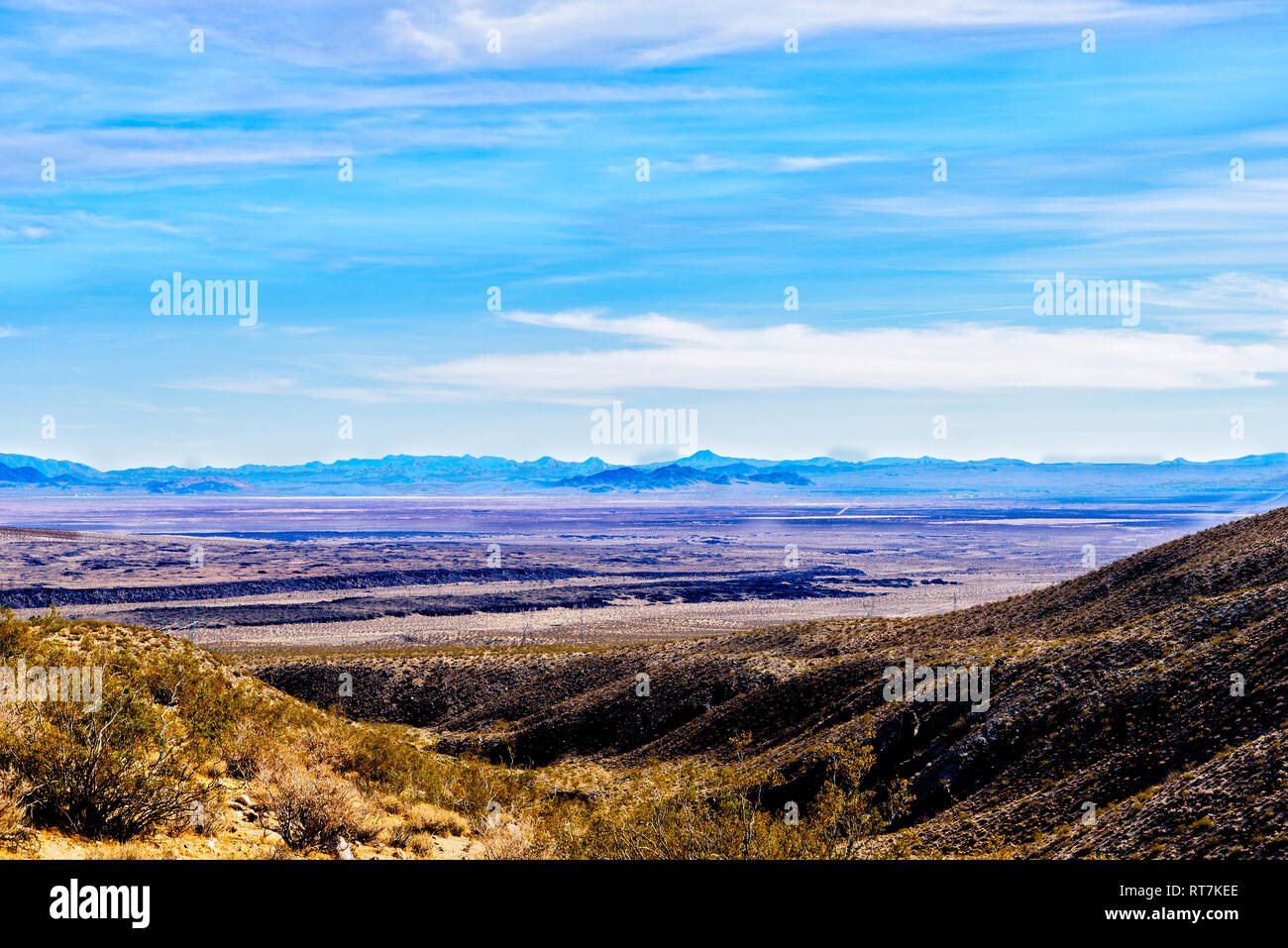 Vu de montagnes du désert à la vallée ci-dessous sous ciel bleu avec des nuages blancs. Les montagnes pourpres, au loin. Banque D'Images