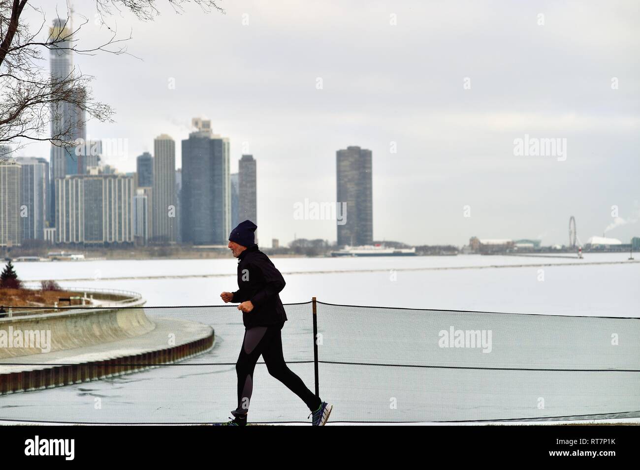 Chicago, Illinois, USA. Un coureur solitaire le jogging le long de la Chicago Museum Campus devant une glace laden le lac Michigan et d'une partie de la ville. Banque D'Images