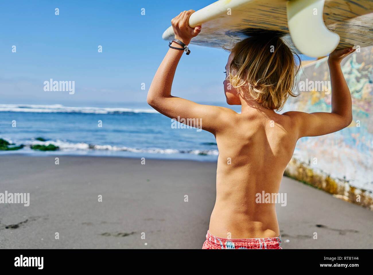 Le Chili, Puerto Maldonado, boy carrying surfboard at the sea Banque D'Images