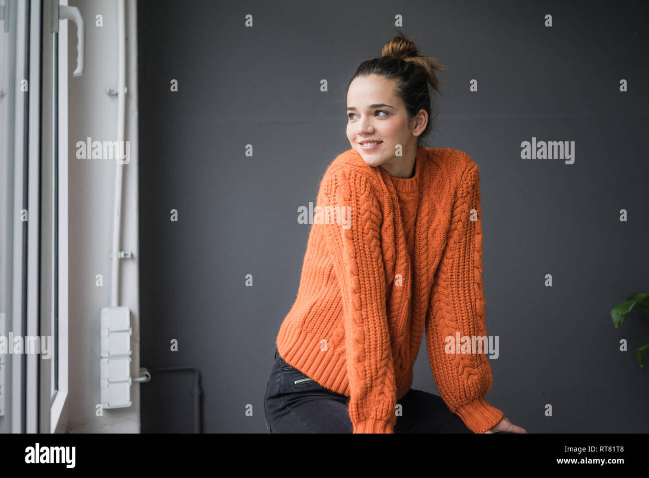 Portrait of smiling woman wearing knit pull orange à la fenêtre de Banque D'Images
