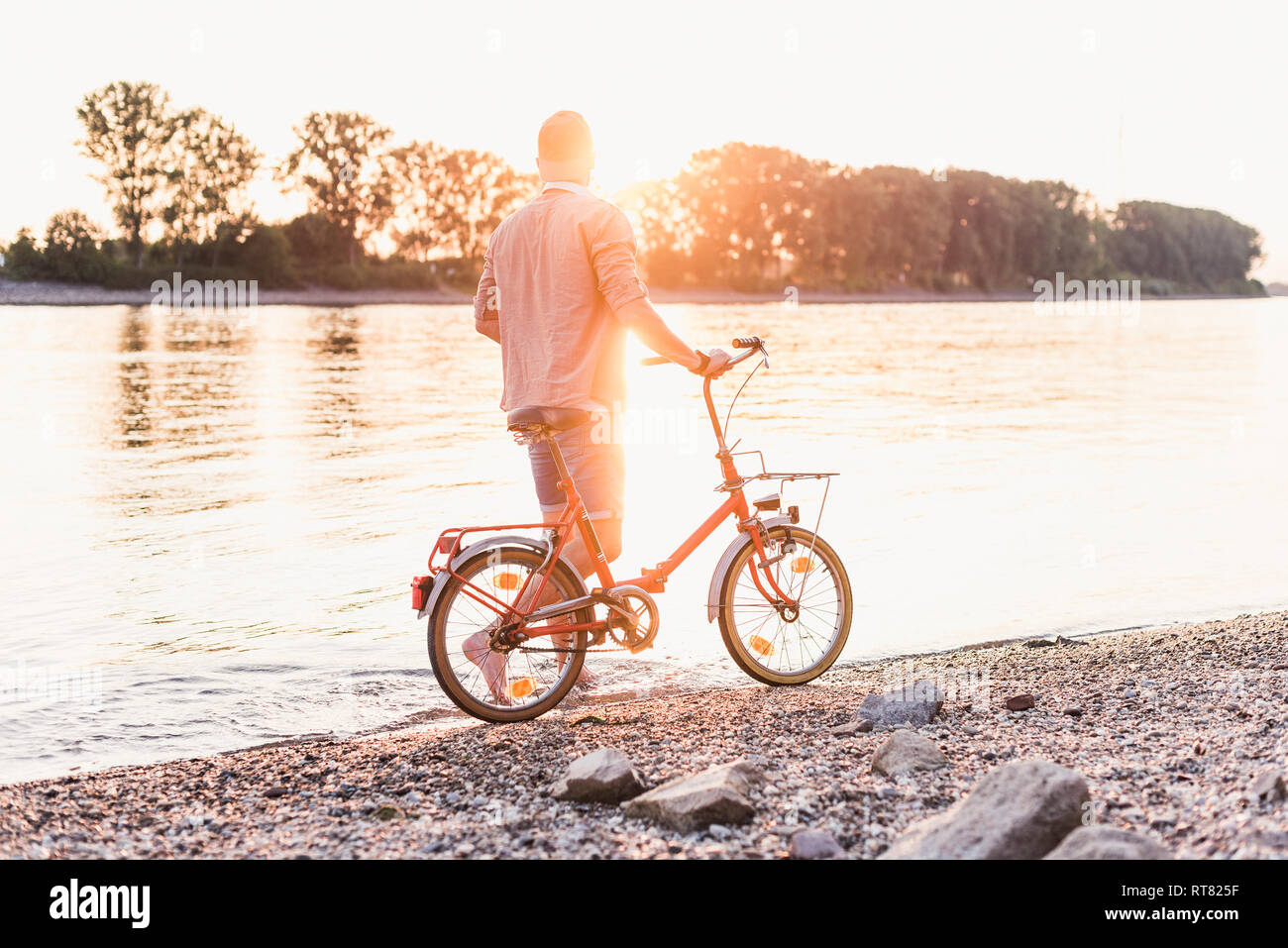 Jeune homme marchant avec vélo à la rivière au coucher du soleil Banque D'Images