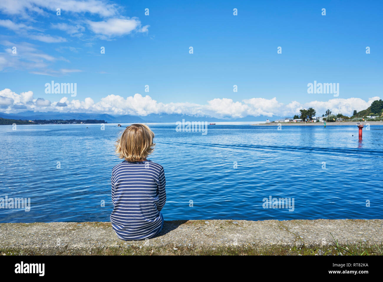 Le Chili, Puerto Montt, garçon assis sur mur de quai au port Banque D'Images