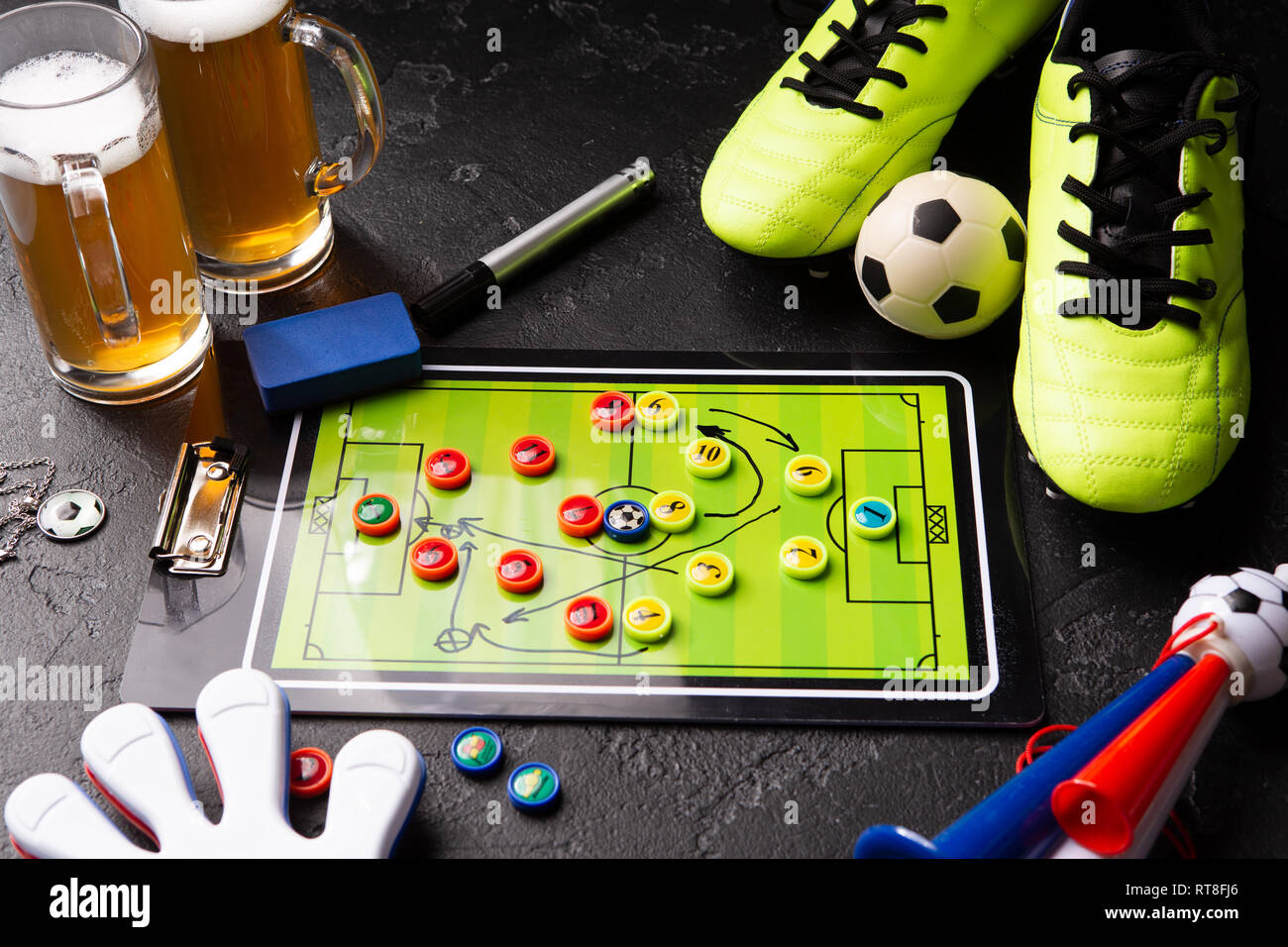 Photo de deux chopes de bière mousse, baby-foot, ballon, chaussures de football, tuyau, jouet hochet Banque D'Images