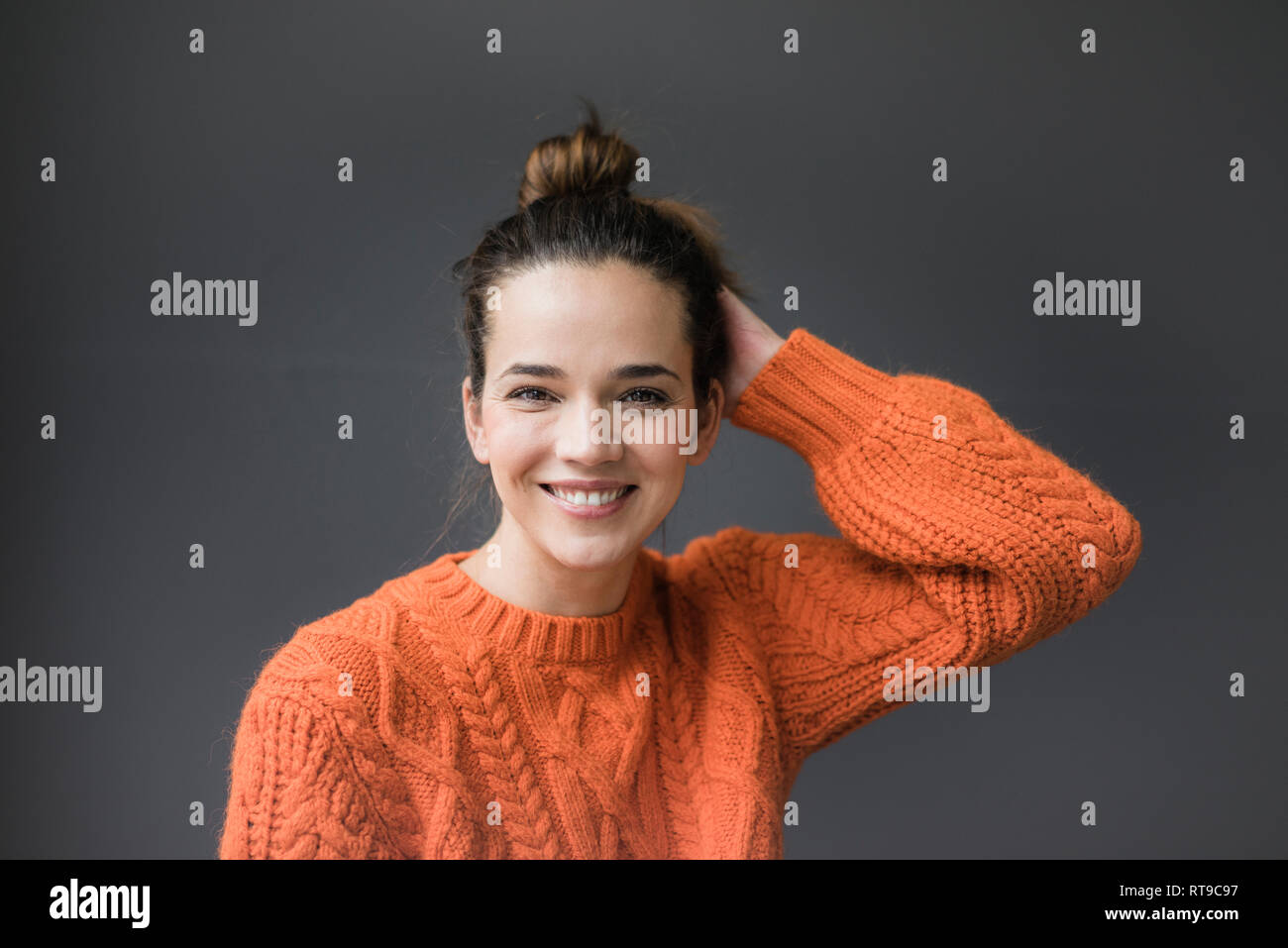 Portrait of happy woman wearing knit pull orange contre l'arrière-plan gris Banque D'Images