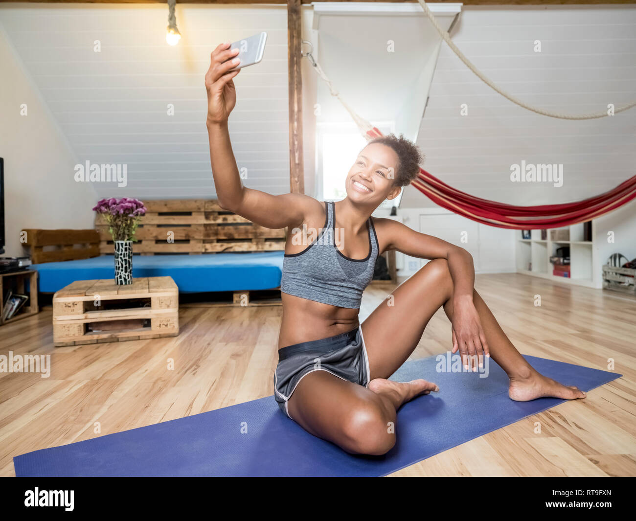 Smiling young woman sitting on yoga mat en tenant un selfies Banque D'Images
