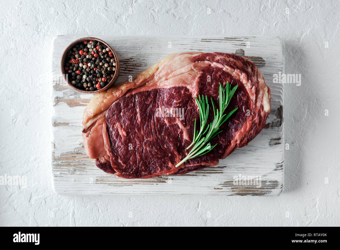Le persillage ribeye steak au poivre et au romarin sur plaque de bois blanc. Hacher la viande de boeuf Banque D'Images