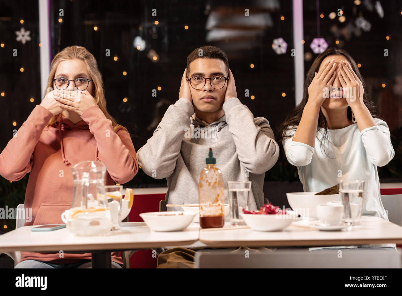 Amis assis dans un restaurant et le faire sur scène trois singes de la sagesse. Banque D'Images