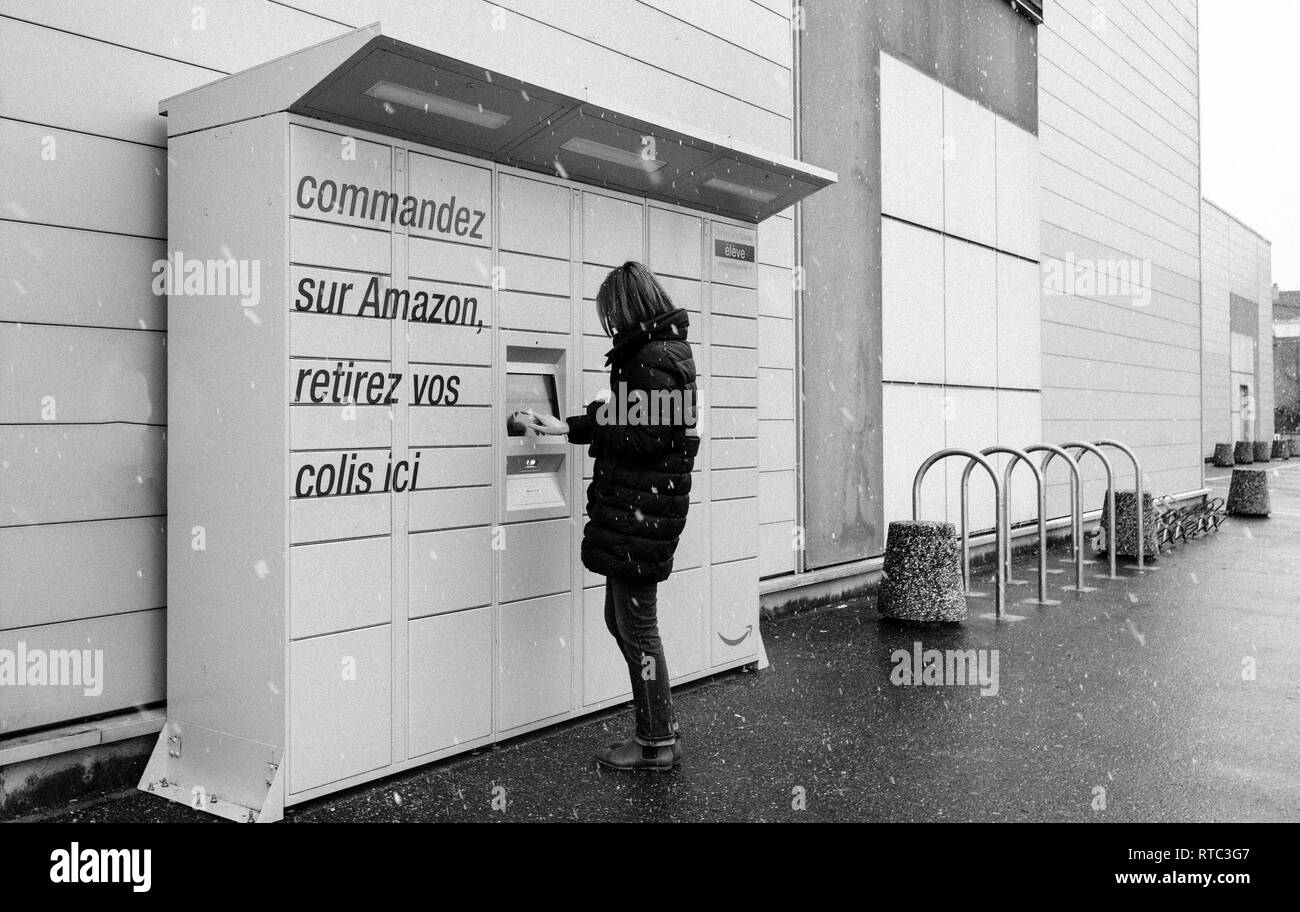 Strasbourg, France - Nov 8, 2018 : side view of young woman using Amazon Locker la livraison de colis en libre-service près de la station service supermarché Auchan Banque D'Images