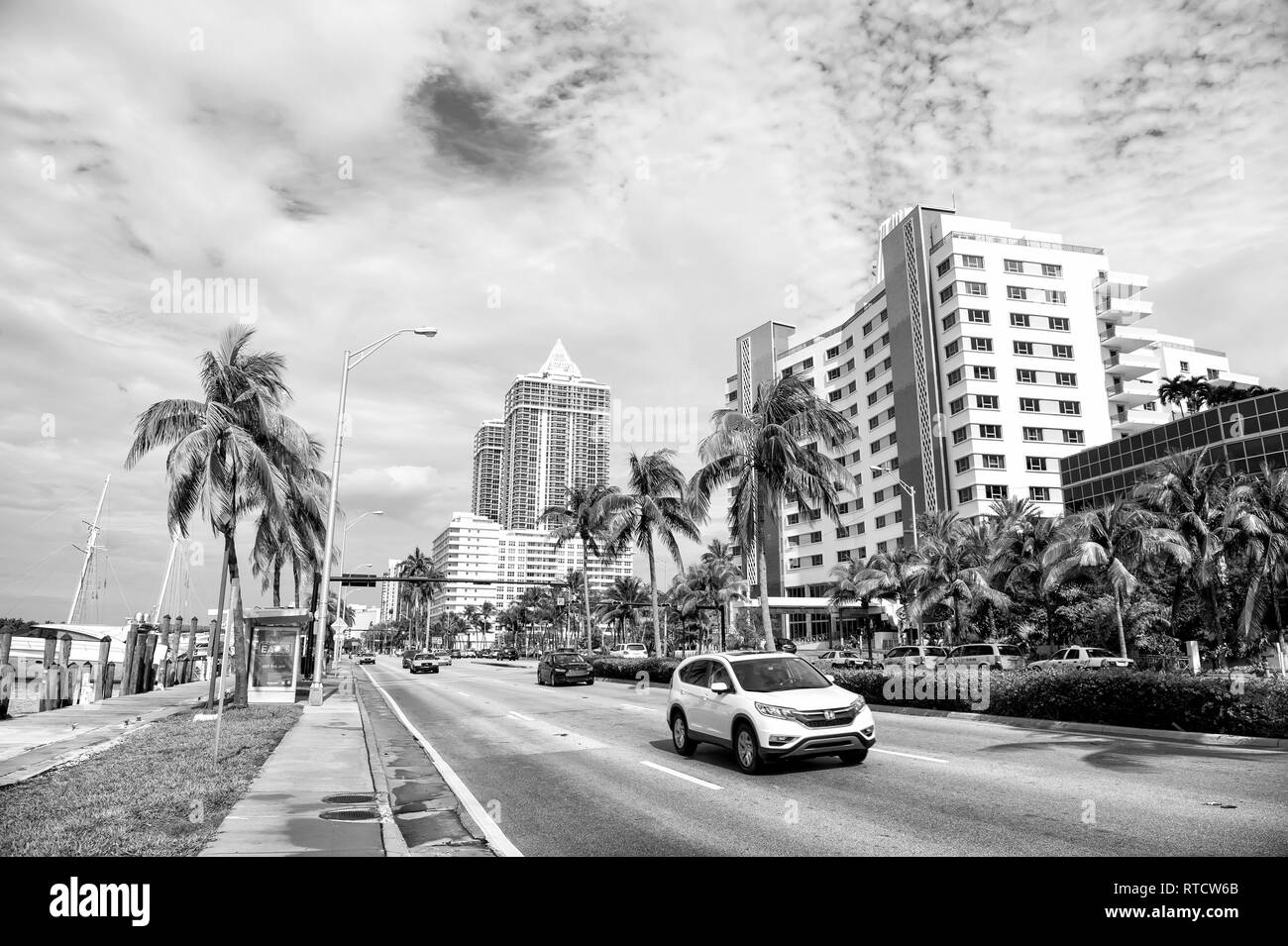 Miami, USA - 10 janvier 2016 : voitures roulant sur route ville le long de la côte de la mer avec des bâtiments modernes, le vert des palmiers et promenade pavée sur fond de ciel nuageux. Le voyage. Des vacances d'été, Colins dur Banque D'Images
