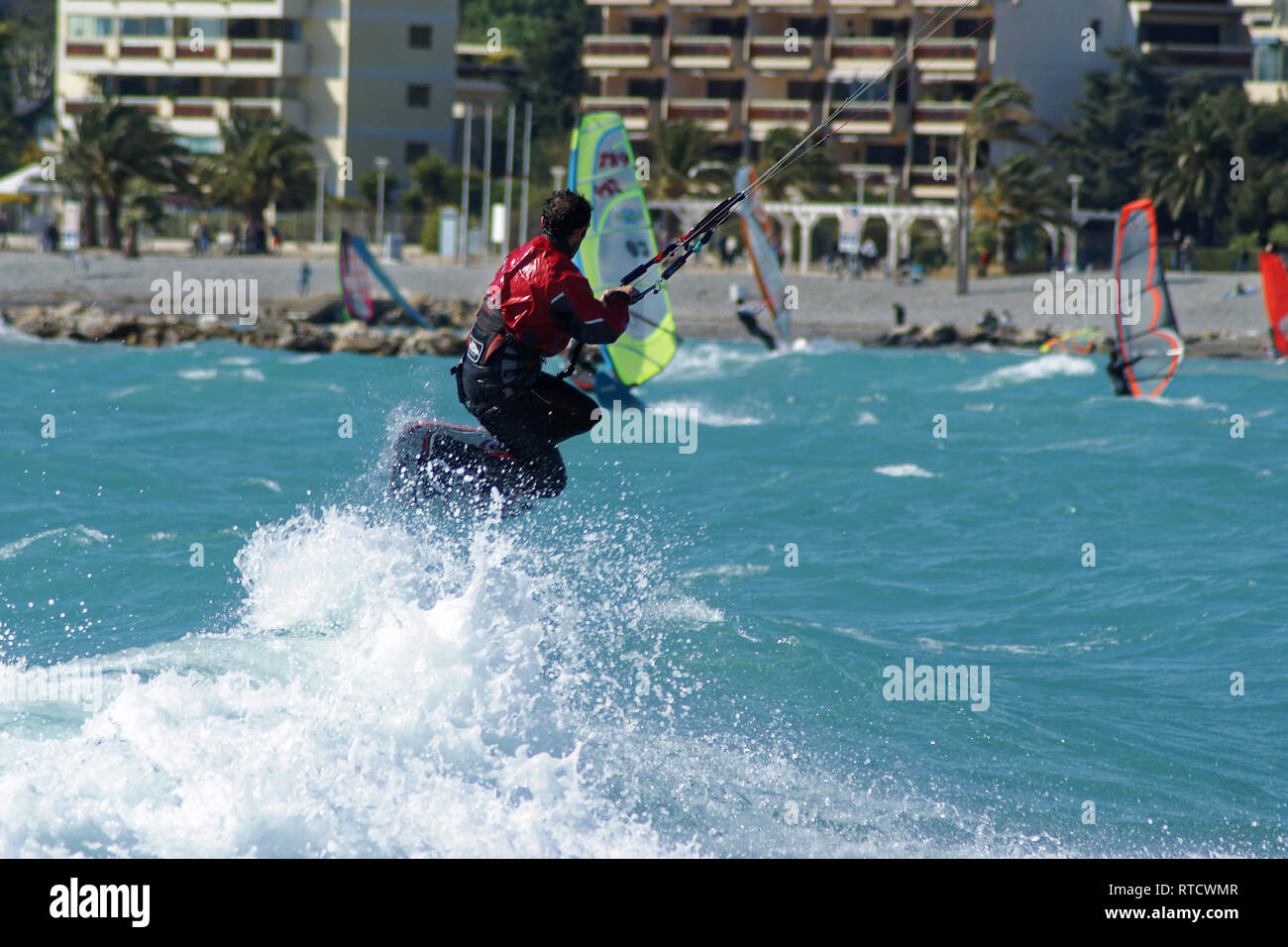 Kiteboarder sautant par dessus la mousse blanche pendant un jour de vent en face de la plage Banque D'Images