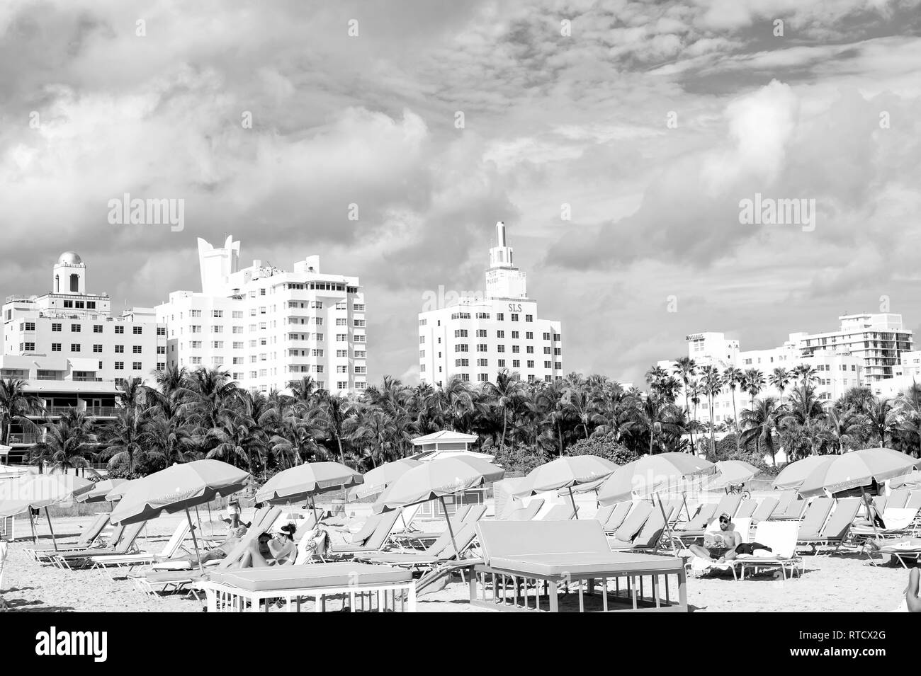 Miami, USA - 10 janvier 2016 : South Beach ou Miami beach. Les gens de vous détendre sur des chaises longues sous des parasols bleus sur la plage de sable ensoleillée avec palmiers, bâtiments élevés sur nuageux ciel bleu. Vacances d'été. Banque D'Images