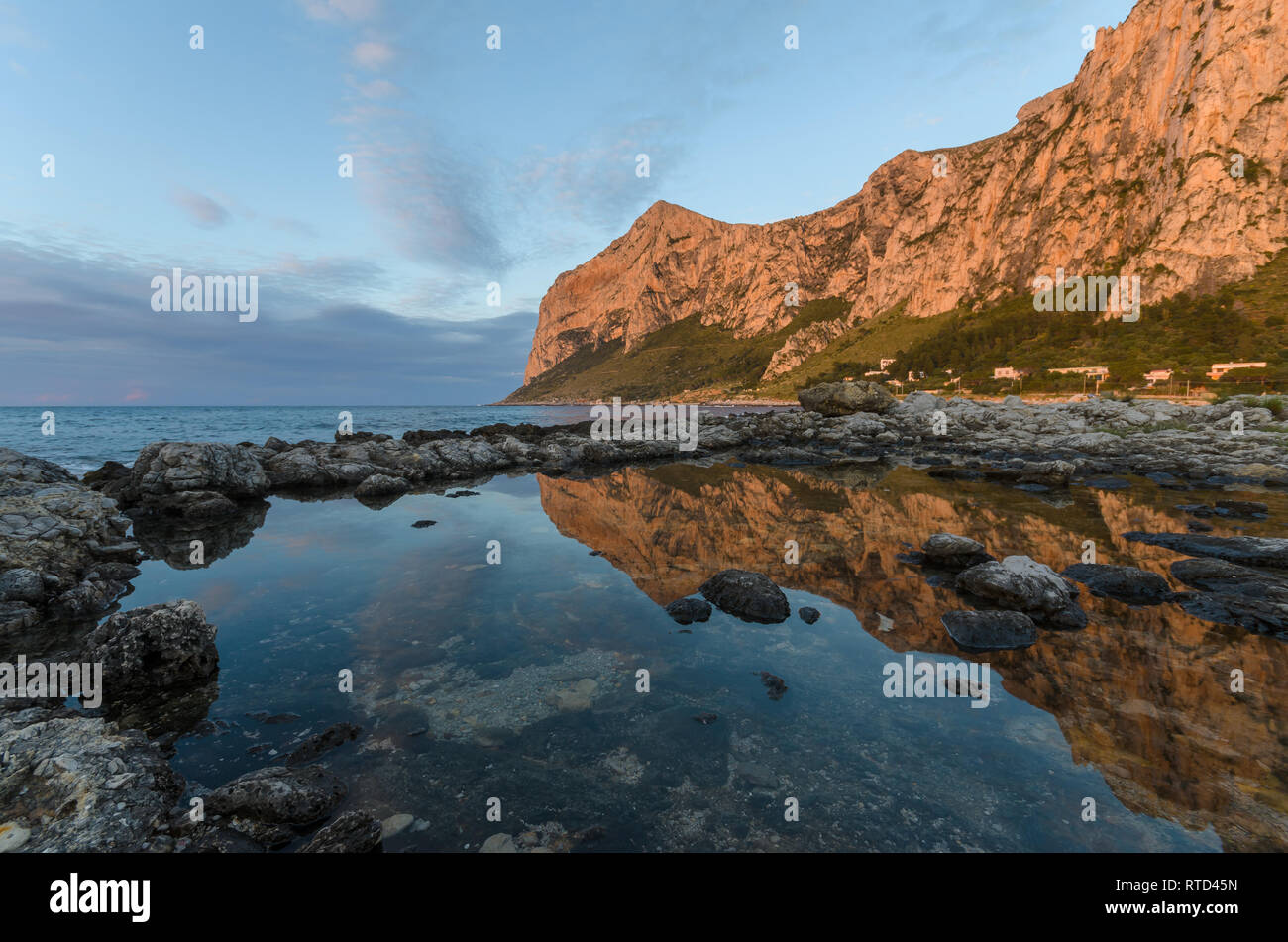 Beaux nuages épars au coucher du soleil à Barcarello, avec le promontoire de Capo Gallo reflétée sur l'eau calme. Palerme, Sicile. Banque D'Images