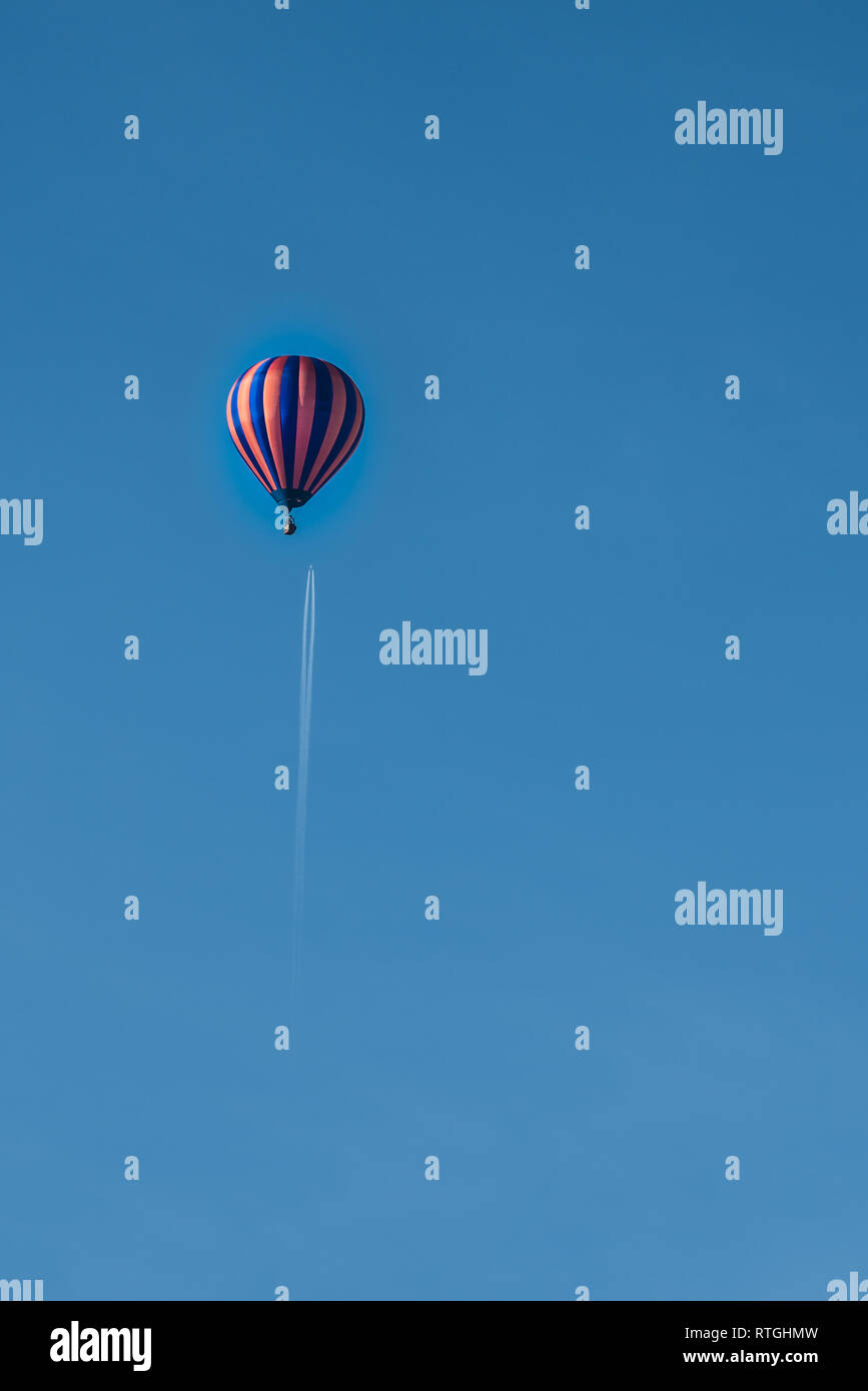 Hot Air Balloon volant sous un jet de passagers et con sentier dans un ciel bleu clair Banque D'Images