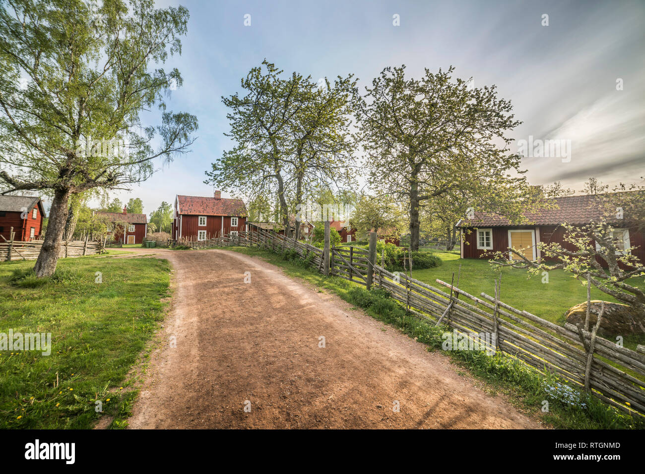 Petite route et vieux chalets traditionnels par roundpole clôture dans un paysage rural au village par Stensjo. Pays-bas, Suède, Scandinavie Banque D'Images