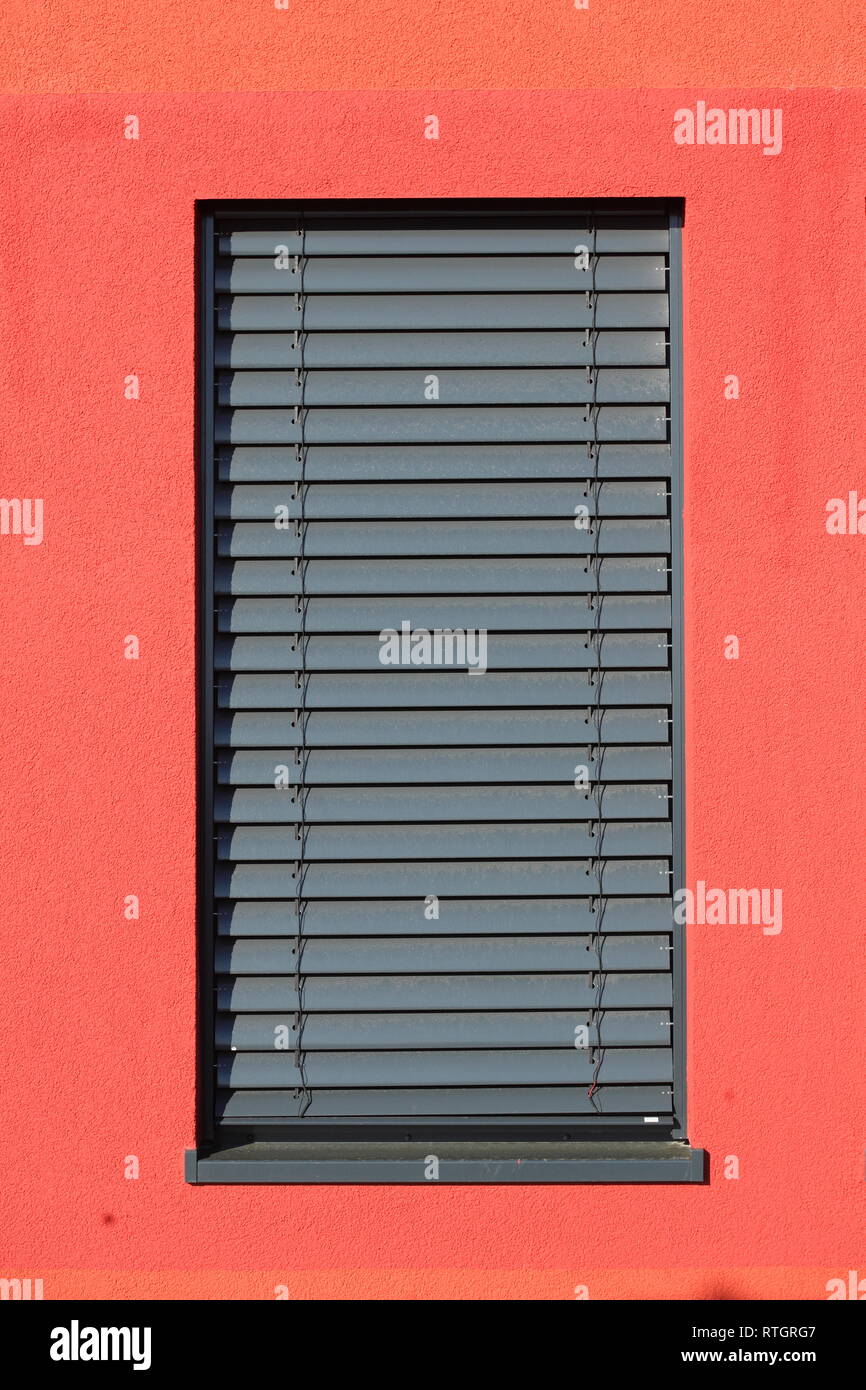 Fenêtre avec stores volets sombre sur un mur de la maison rouge Banque D'Images