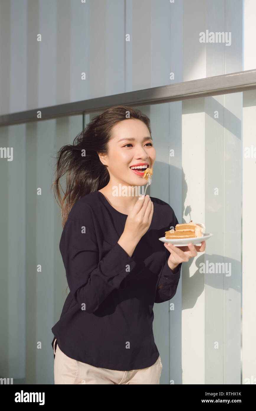 Jeune femme heureuse se tient sur la terrasse de l'hôtel avec des gâteaux dans la matinée. Jolie fille asiatique dans la bonne humeur et est prêt pour l'aventure. Banque D'Images