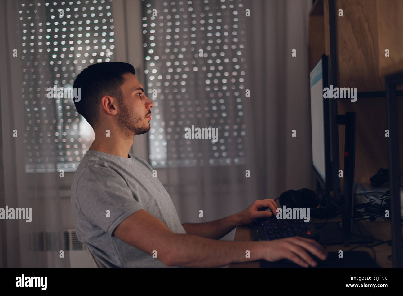 Programmeur travaille sur son ordinateur lorsque l'écran reflète la lumière sur son visage. Banque D'Images