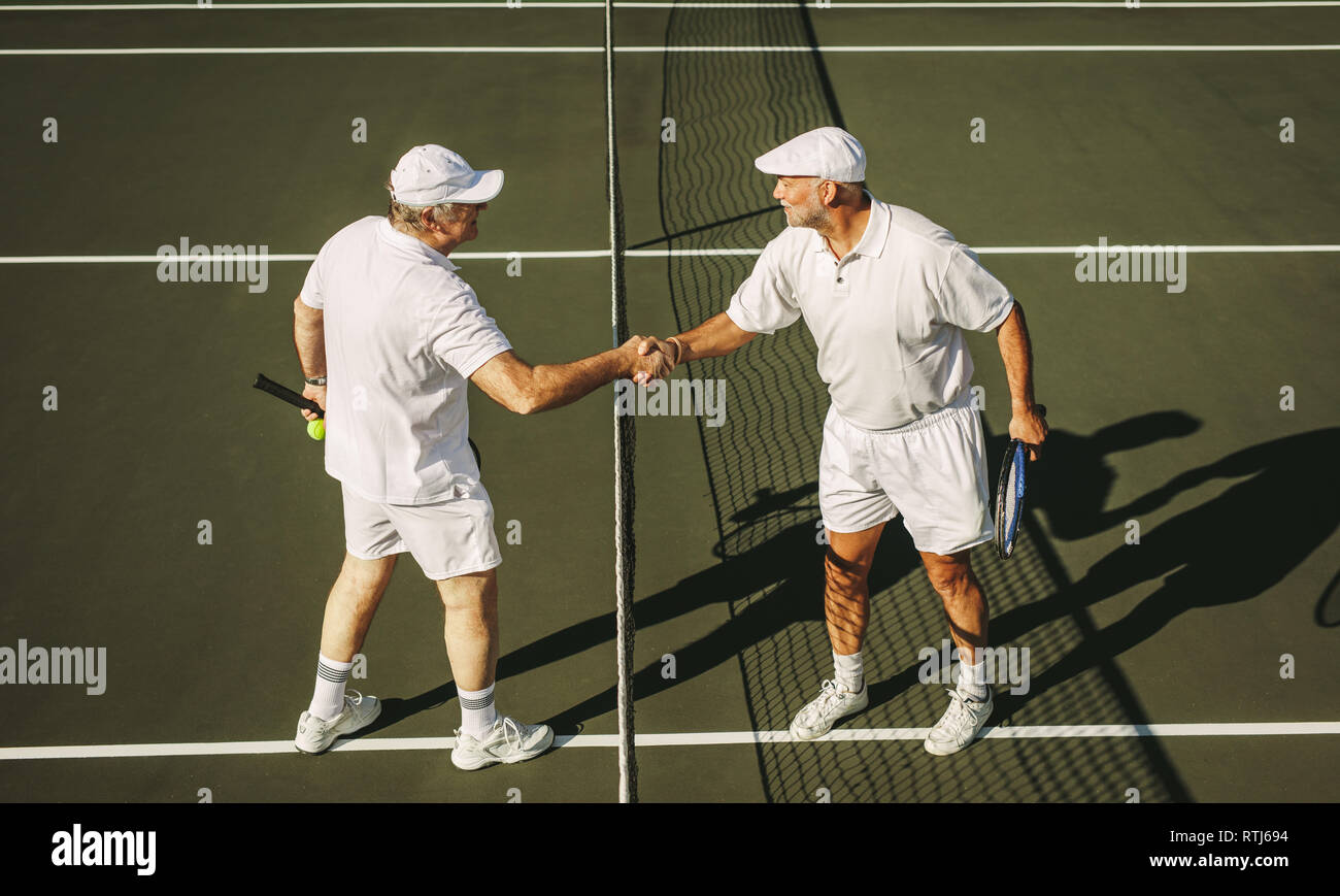 Vue latérale des deux joueurs de tennis senior se serrer la main sur un court de tennis. Les hommes sur un court de tennis, debout près de la poignée de mains nettes. Banque D'Images