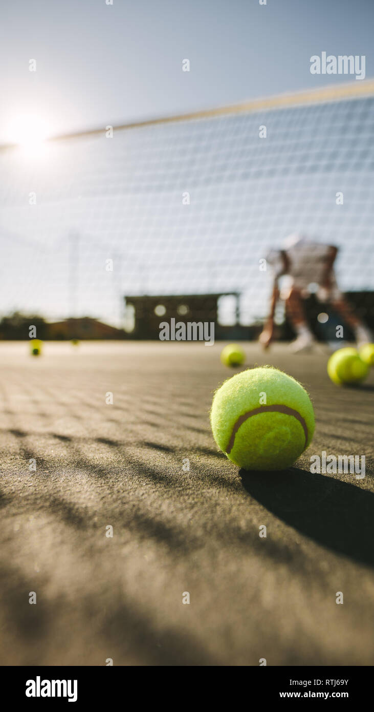 L'homme jouant au tennis sur une journée ensoleillée avec des balles de tennis se trouvant sur la cour. Gros plan d'une balle de tennis sur le sol. Banque D'Images