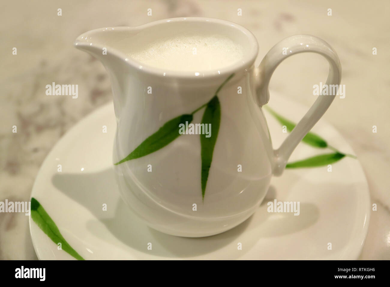 Blanc avec motif de feuilles vert pichet de lait sur une soucoupe Banque D'Images