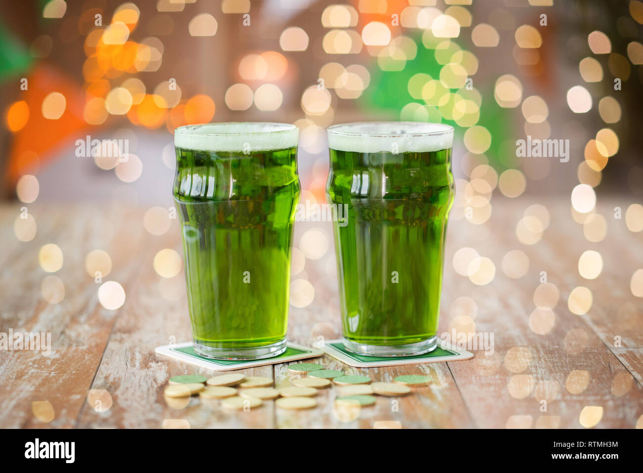 Verres de bière verte et de pièces d'or sur la table Banque D'Images