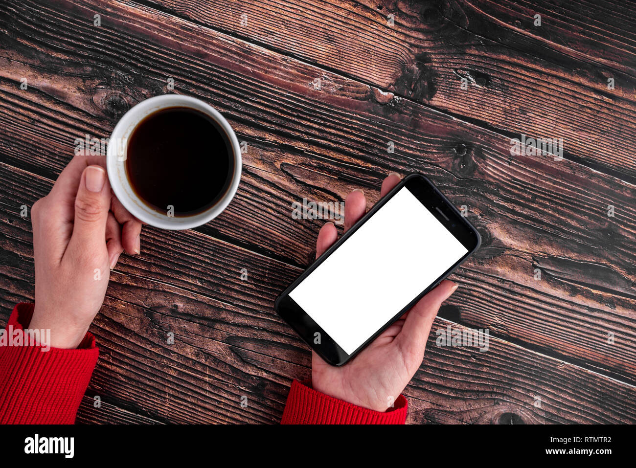 Porter du rouge femelle cavalier, ses mains tenant cellulaire et un café sur fond de bois Banque D'Images